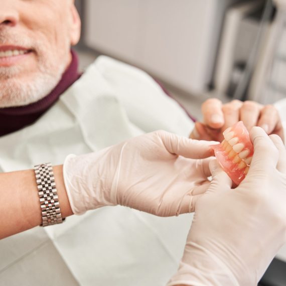 Its my new teeth. Cropped view of the dentist showing to senior grey haired patient teeth dentures while working at the dental clinic. Man sharing satisfaction smile